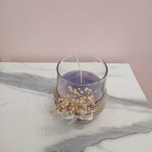 Vela morada en vaso de vidrio con flores secas